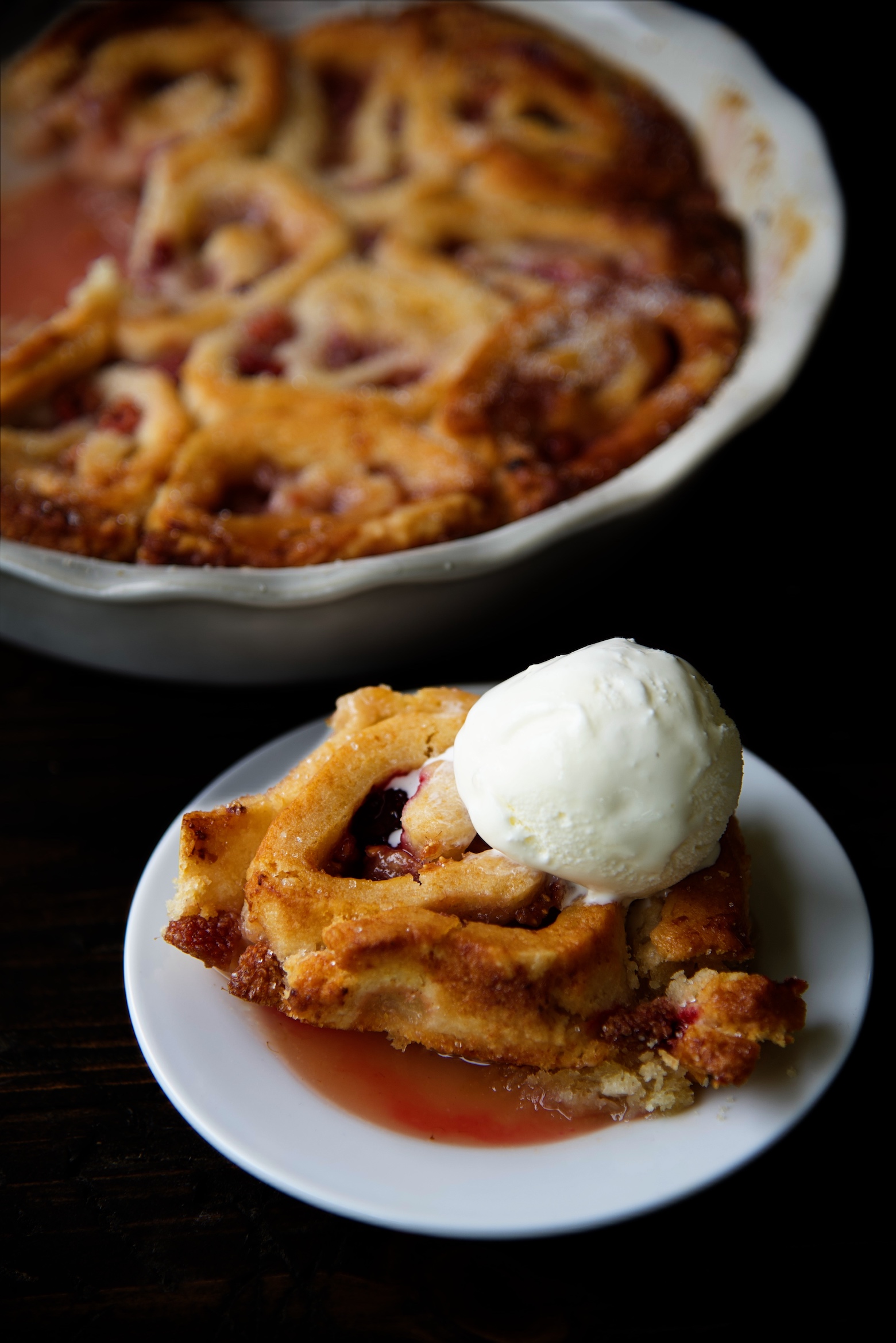 Cobbler piece on a plate with a scoop of ice cream with remaining cobbler in background.