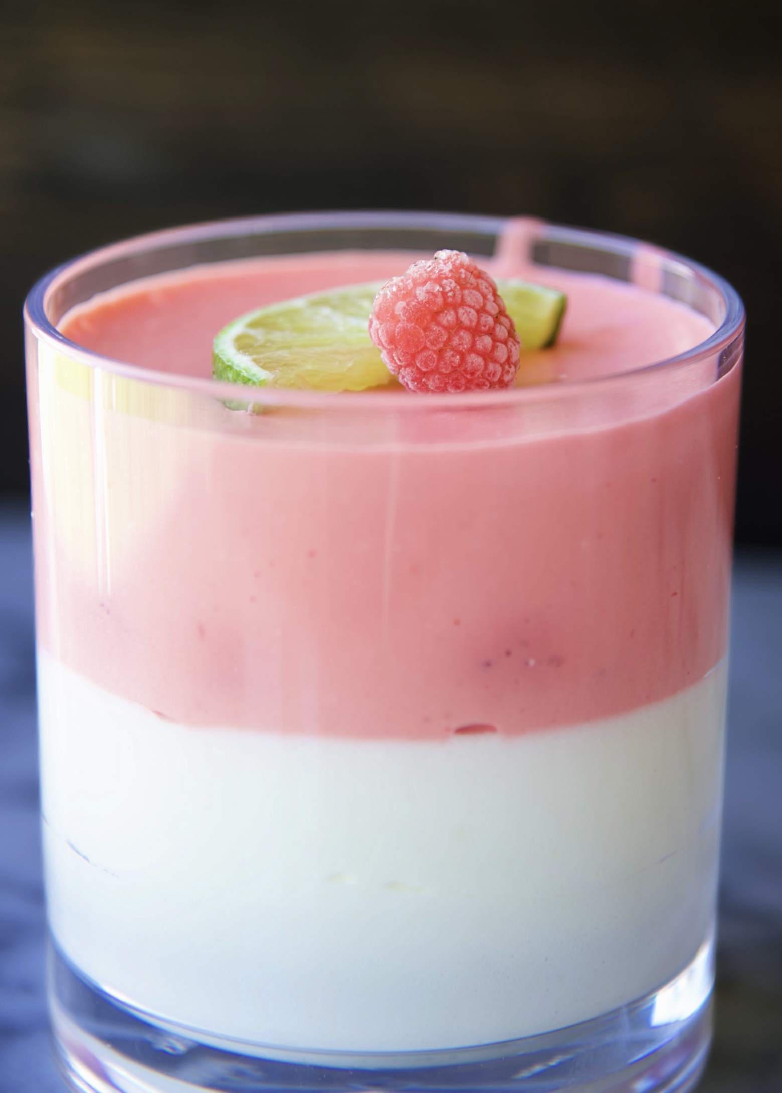 Close up of a glass with 1/2 margarita jello layer and 1/2 with a raspberry layer. Topped with raspberry and lime slice.