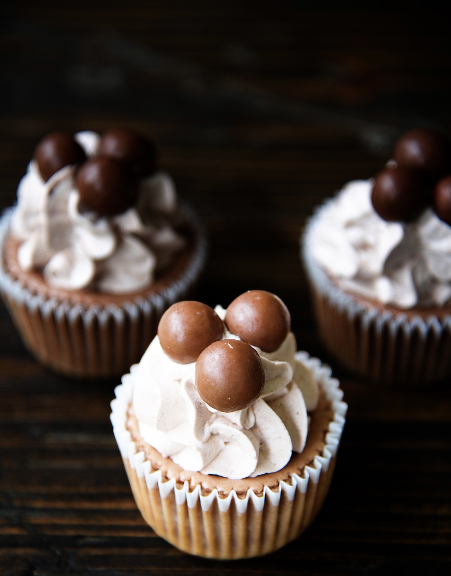 Cluster of three Malt Cup Cheesecake Bites with focus on the first cheesecake bite with whipped cream and three malted milk balls. 