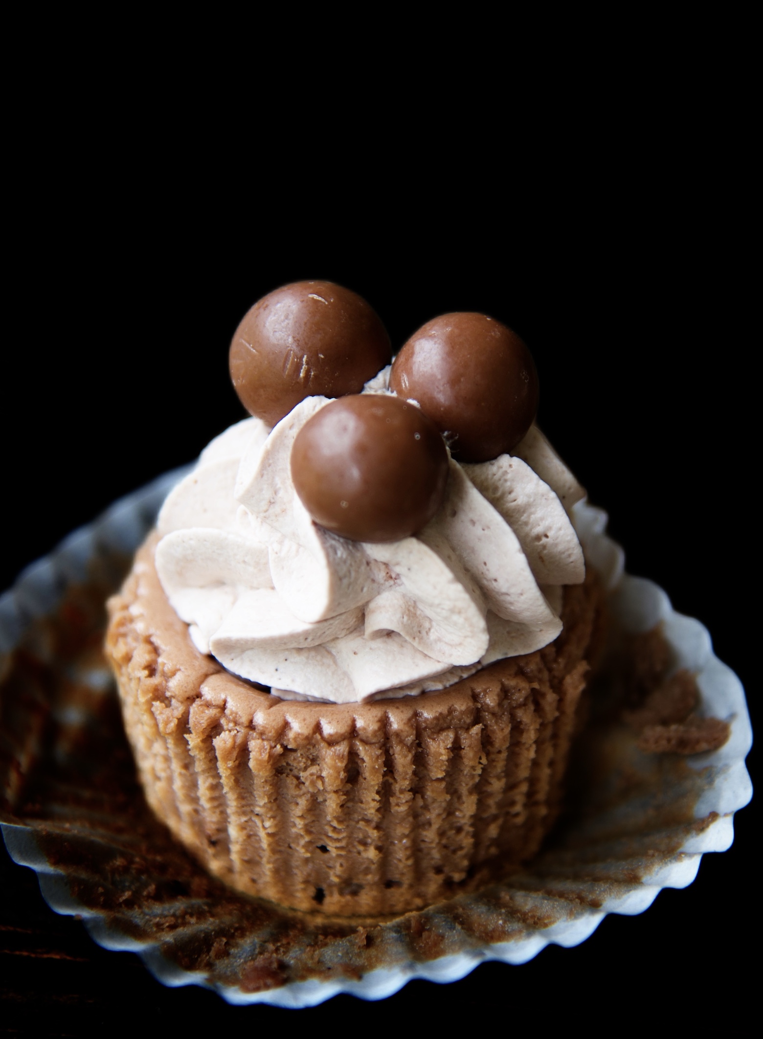 Single Malt Cup Cheesecake Bite with the cupcake liner pulled down and with a focus on the whipped cream and malted milk balls. 