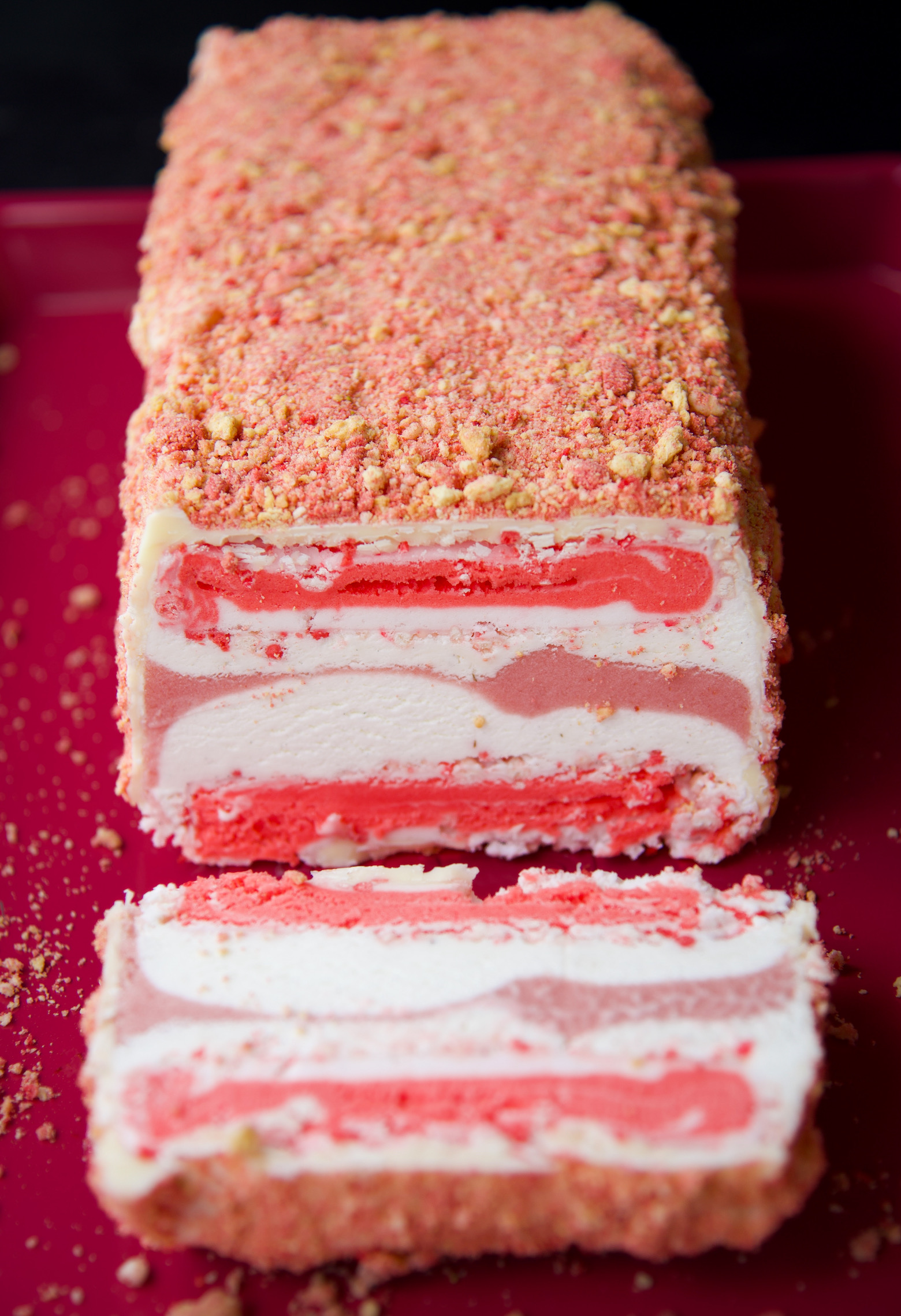 Strawberry Shortcake Ice Cream Terrine with a slice cut out of it which is laying in front of the rest of the terrine. 