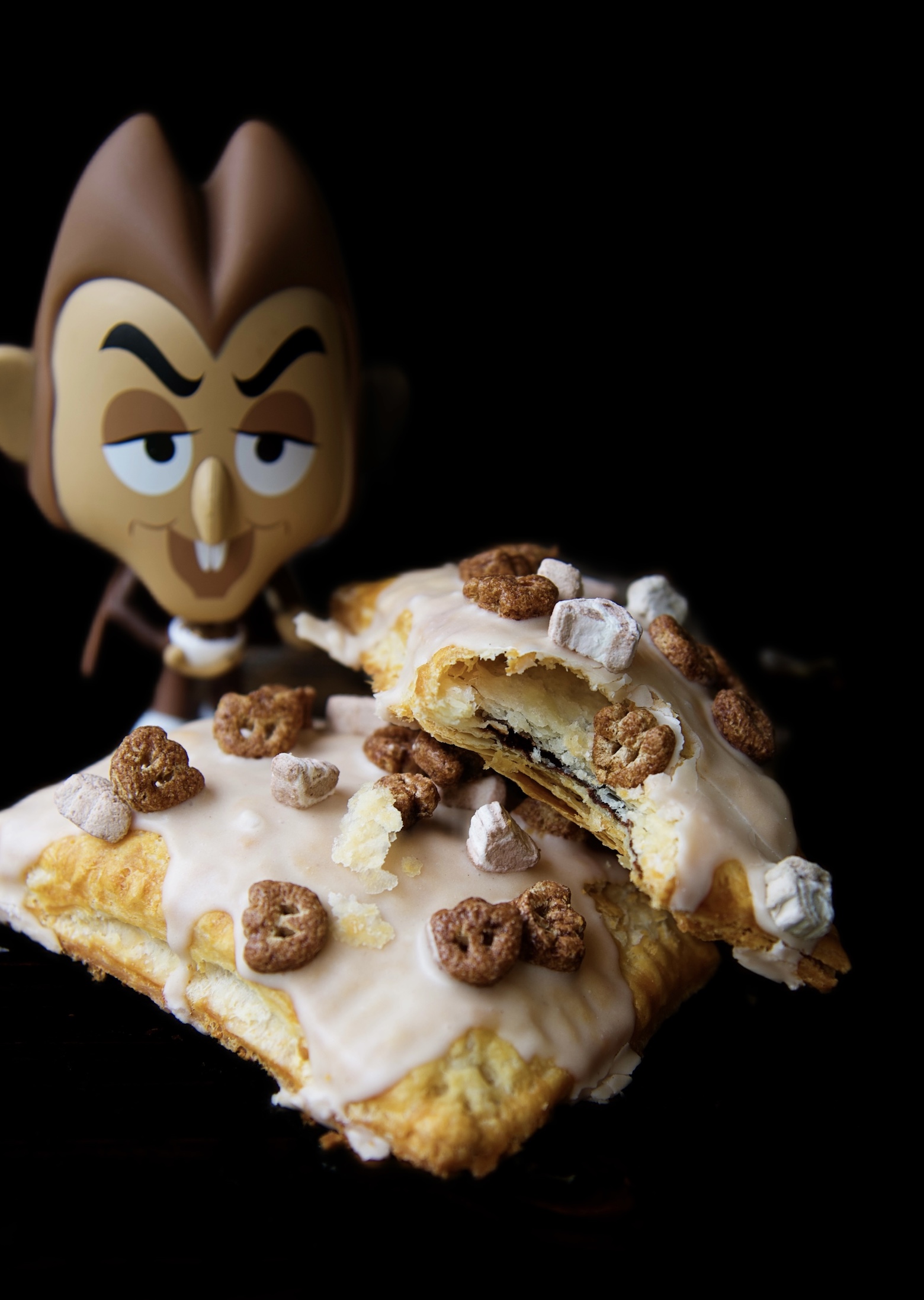 Two Count Chocula Pop Tarts stacked on top of each other. One pop tart has a bite out of it exposing the filling. Count Chocula figurine in the background. 