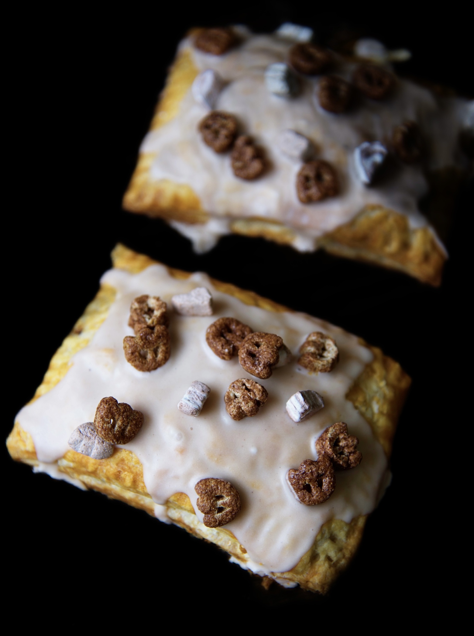 Two Count Chocula Pop Tarts, the one in front has the focus on it. With the chocolate icing and cereal pieces on top. 