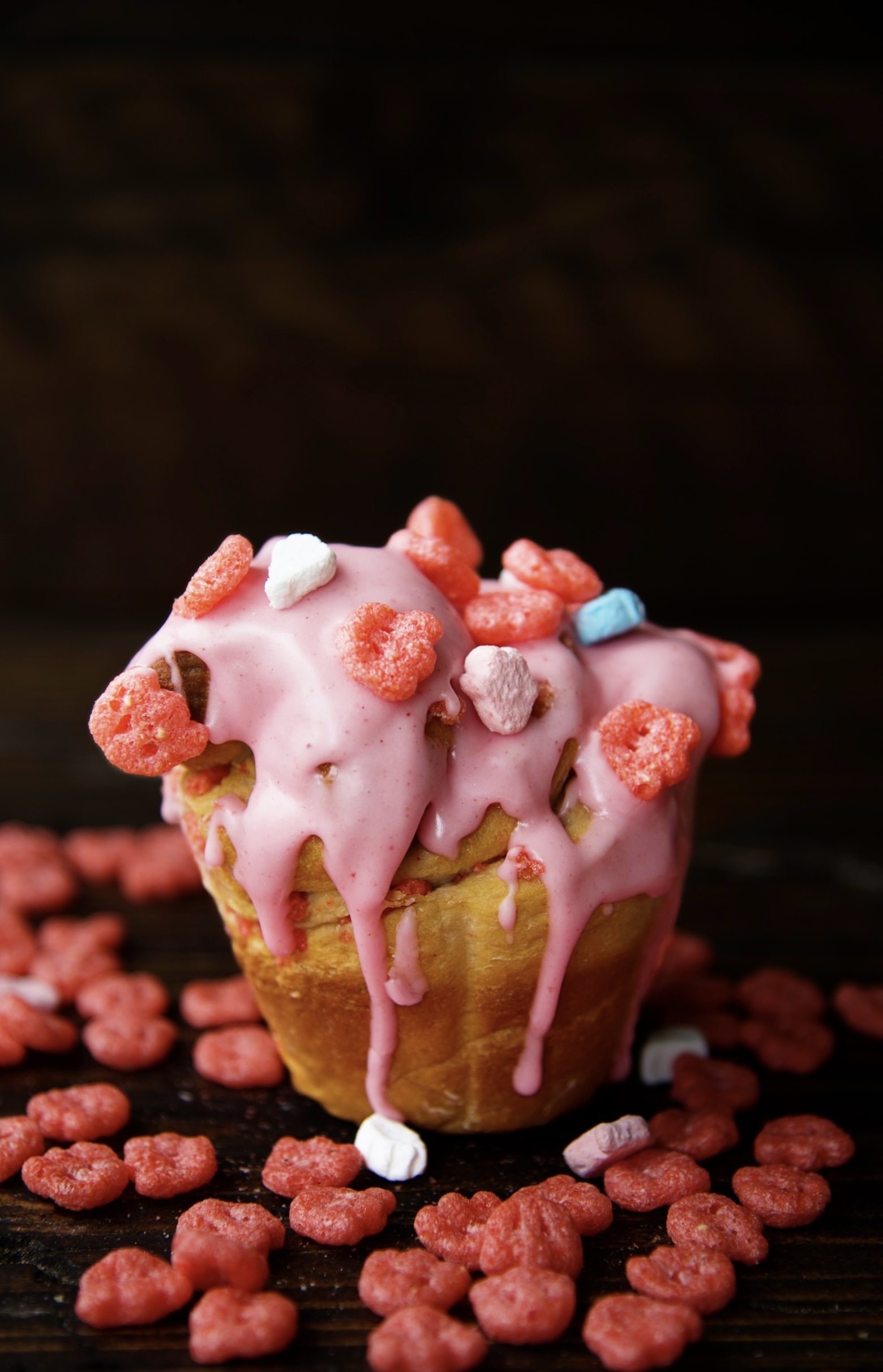 Single Franken Berry Breakfast Bun with pink glaze dripping down and topped with Franken Berry cereal. 