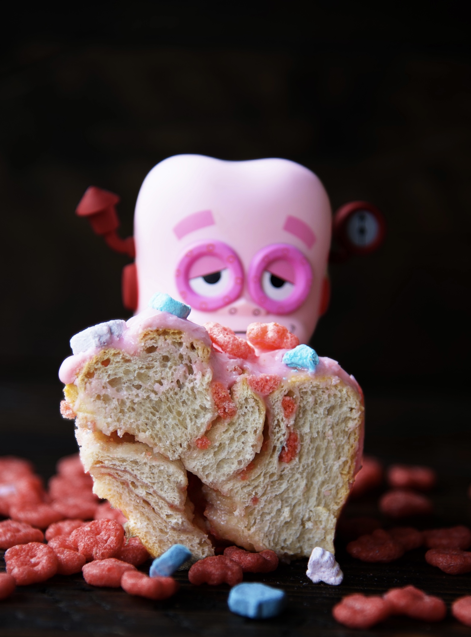 Franken Berry Breakfast Bun cut in half exposing crumb structure. Franken Berry figurine behind it.