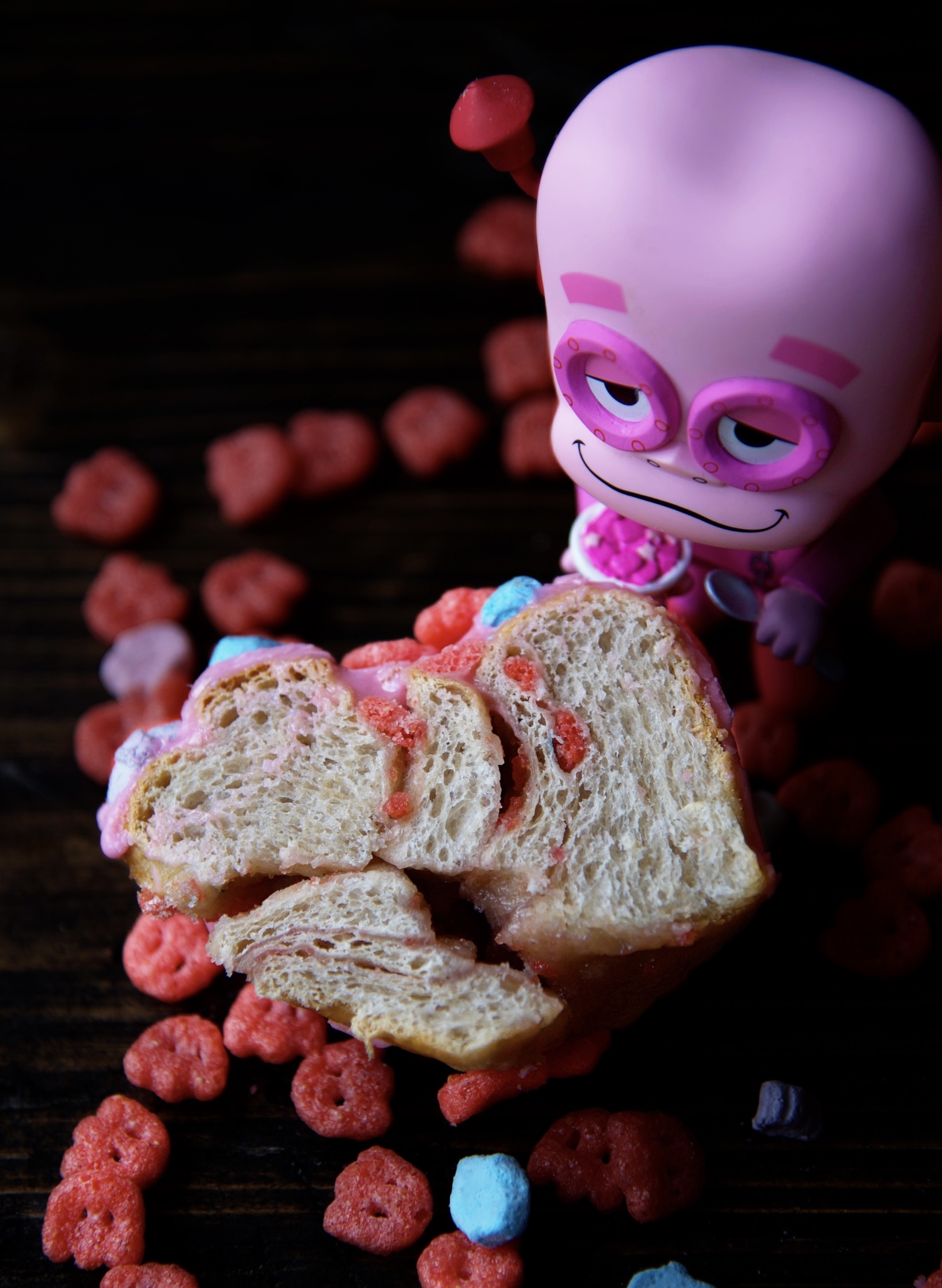 Franken Berry Breakfast Bun cut in half and facing upward exposing crumb structure. Franken Berry figurine next to it