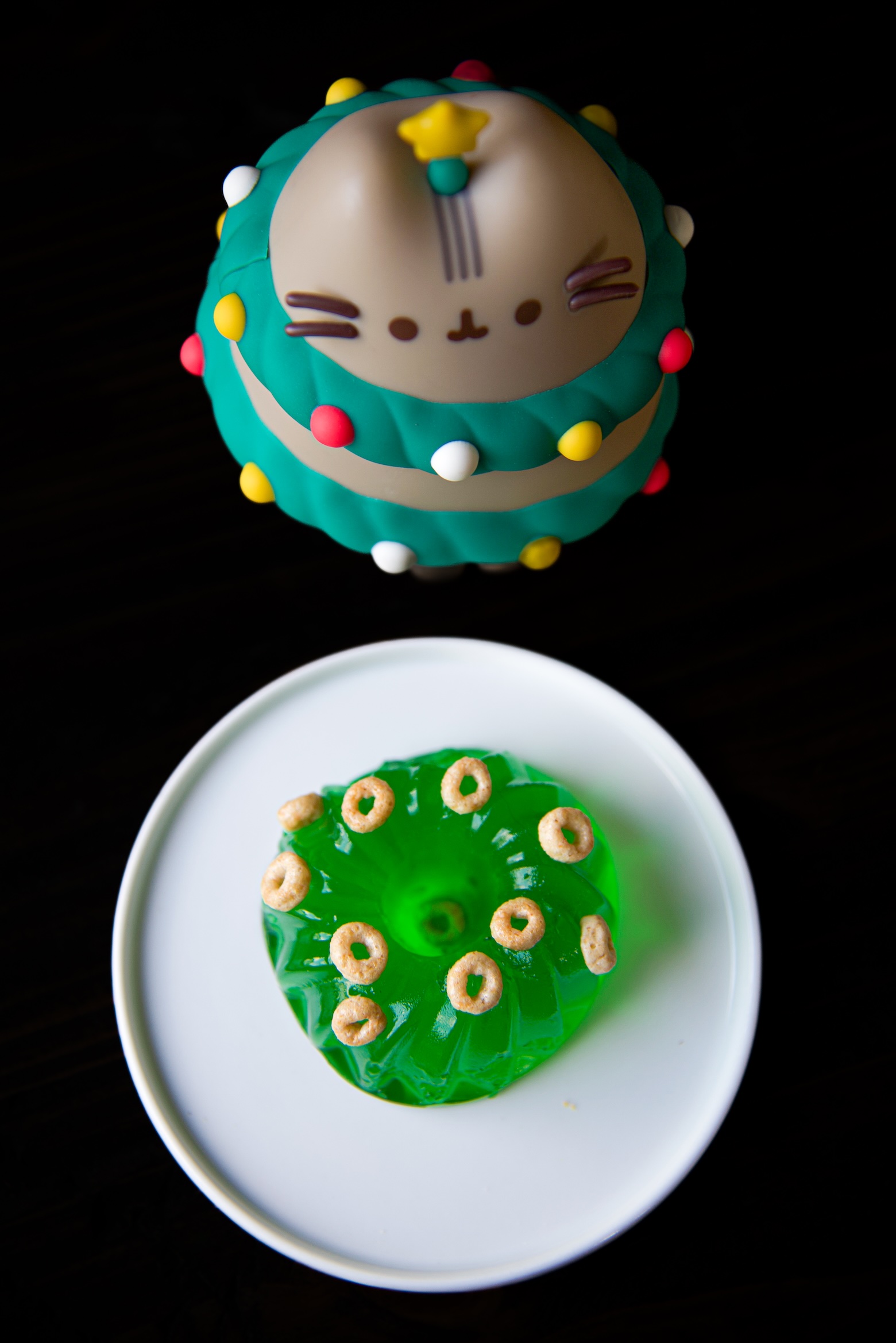 Overhead shot of mini green jello mold with mini cereal scattered on top with cat as a christmas tree in background. 