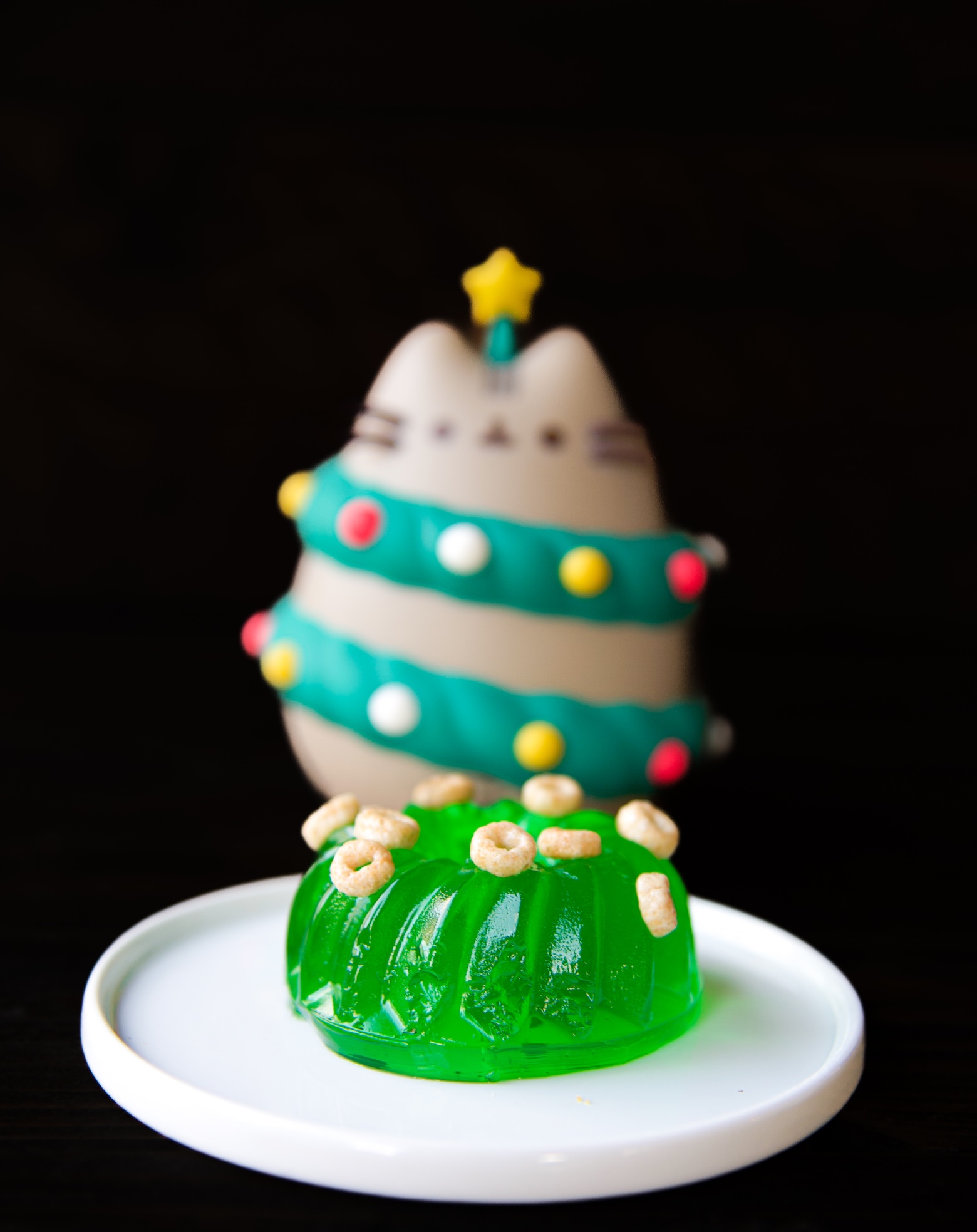 Mini green jello mold with mini cereal scattered on top with cat as a christmas tree in background. 