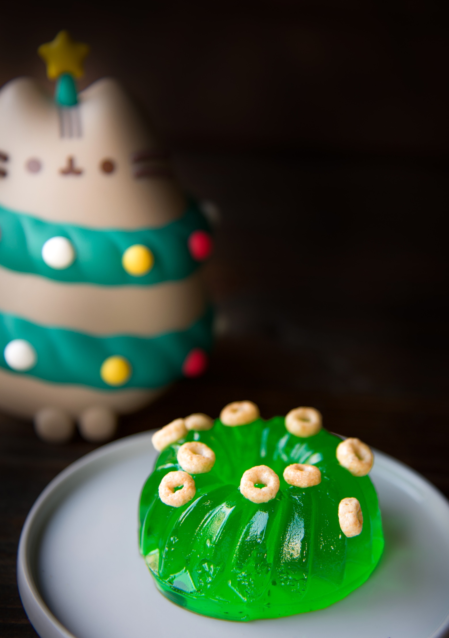 Mini green jello mold with mini cereal scattered on top with cat as a christmas tree to the left of the jello mold.