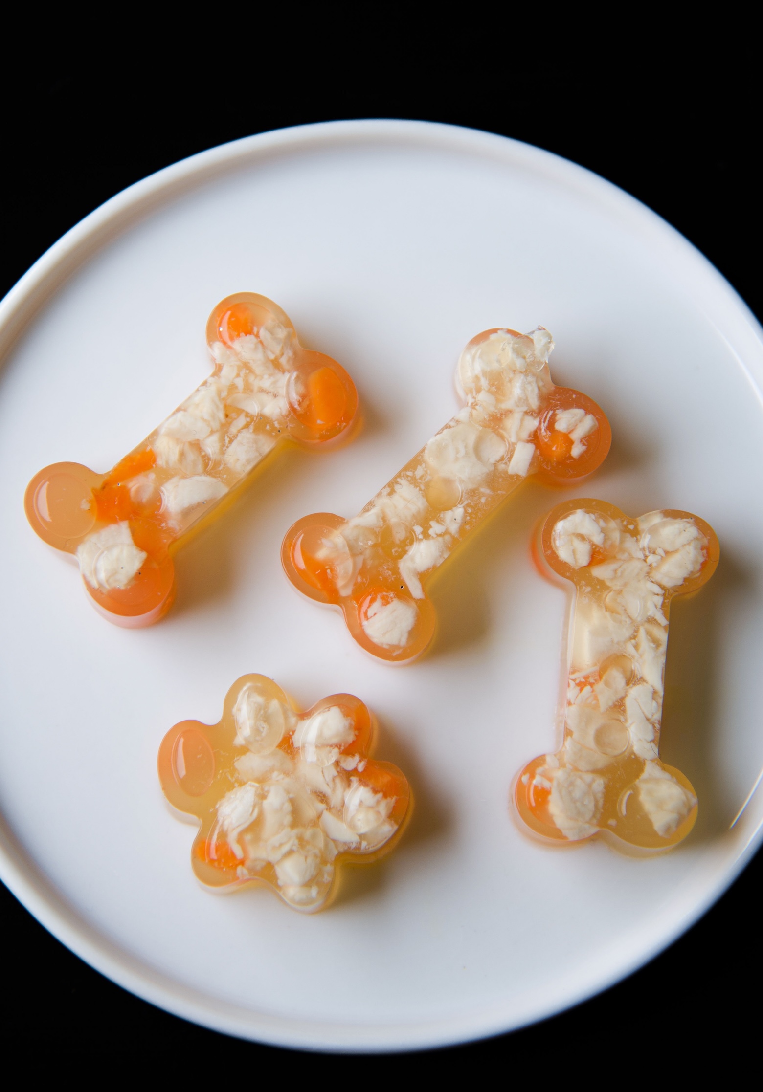 Overhead shot of three chicken jello shot bones and one jello shot paw on a small white plate. You can see the chopped up chicken and carrots. 