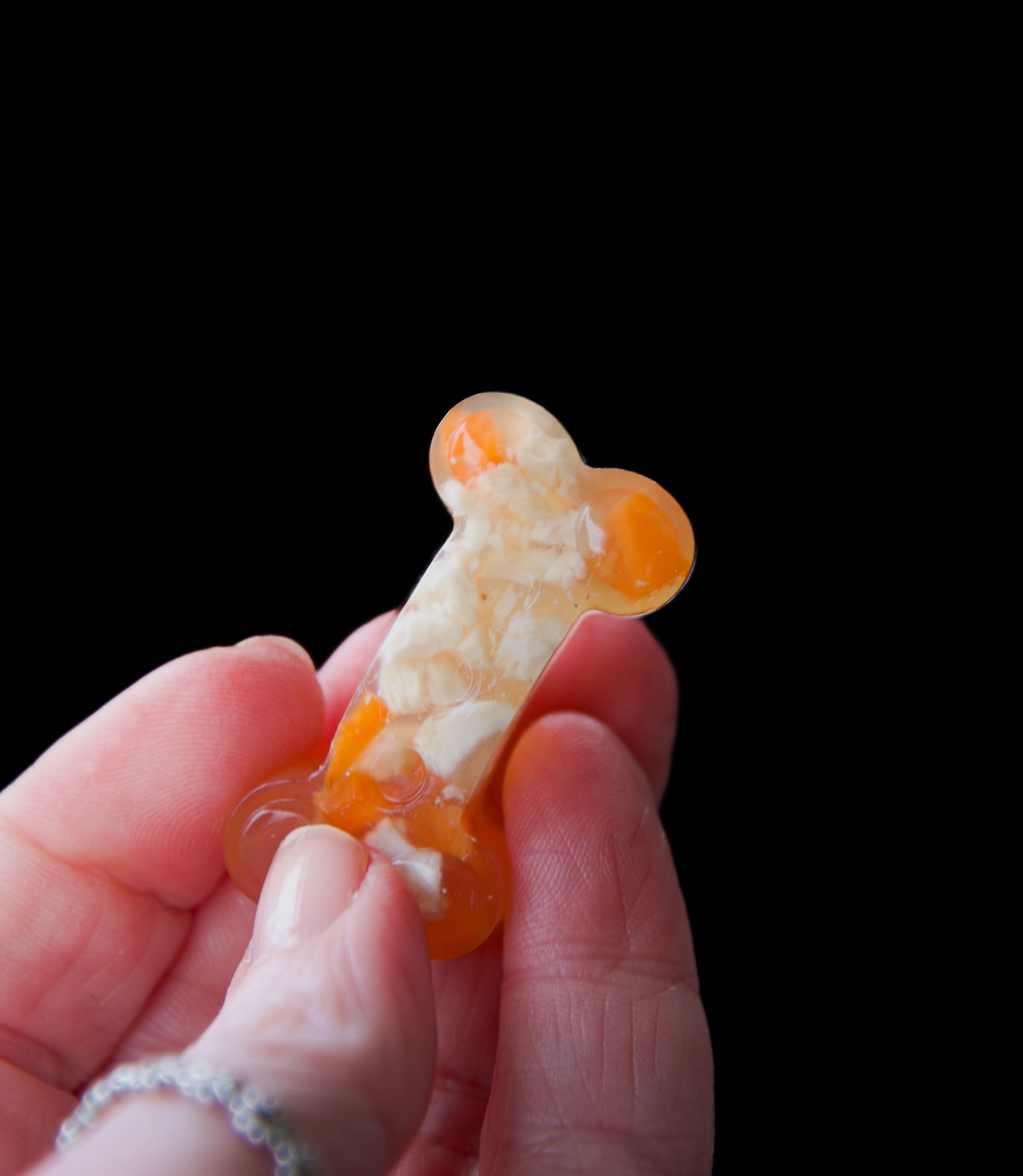 Close up of a chicken jello shot bone being held in a hand by fingers. You can see the chicken and carrot pieces inside. 